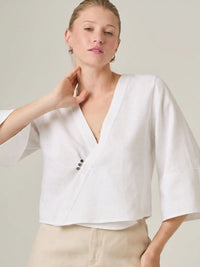 Blusa blanca elegante con mangas amplias que aportan movimiento y frescura. Su diseño cruzado la convierte en una prenda femenina y versatil, ideal para outfits casuales elegantes o de oficina.