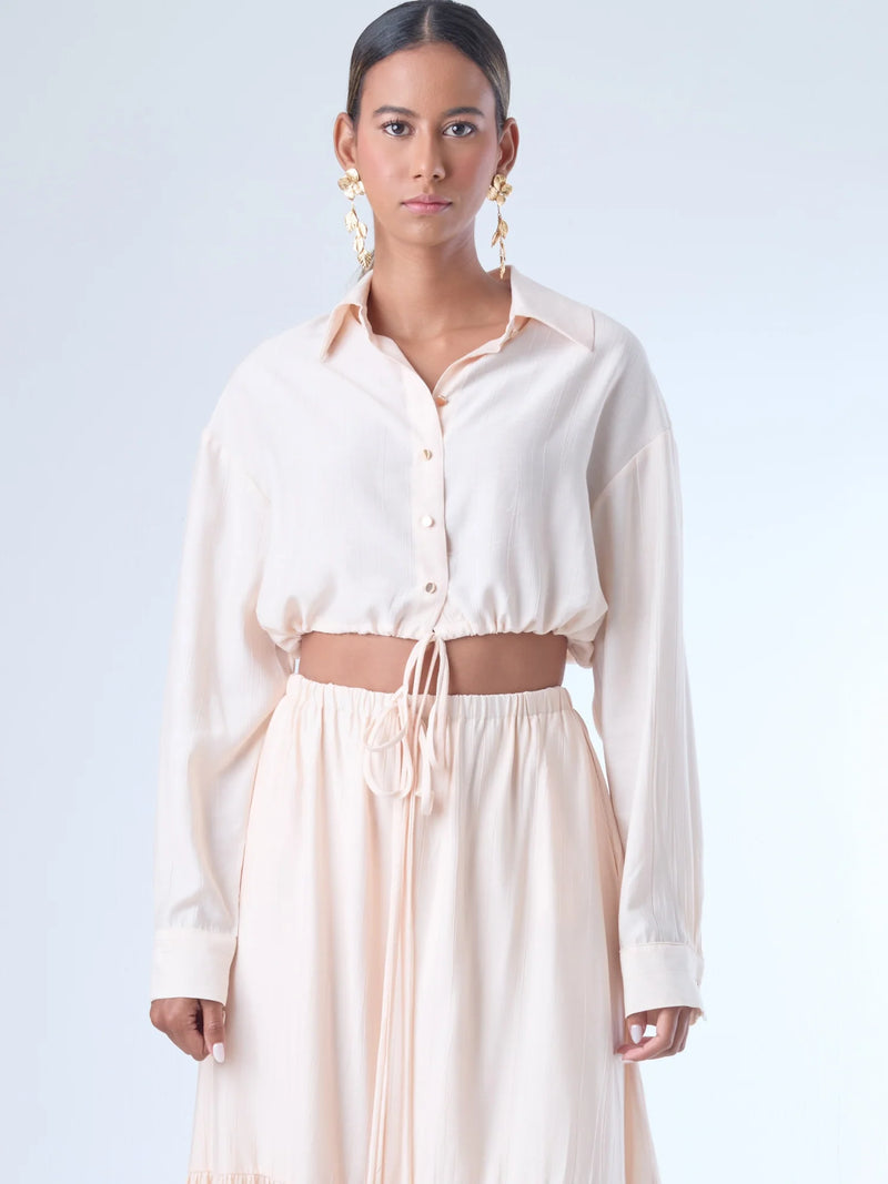 Blusa de corte relajado y largo cropped, con manga larga y puños con botones. Tiene cuello clásico camisero y una botonadura frontal. La prenda se ajusta a la cintura mediante un ligero fruncido con cordón interno, creando un efecto ablusado. Su estilo es casual con un toque sofisticado y femenino.

Detalles:

Color: Curuba

Material:18% Nylon 82% Rayón