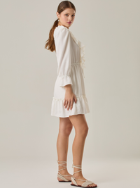 Vestido corto con volantes en el escote en V y en el ruedo. Tiene mangas largas con puños fruncidos y ajuste en la cintura con cordón. Su estilo femenino y romántico lo hace ideal para ocasiones casuales con un toque delicado.