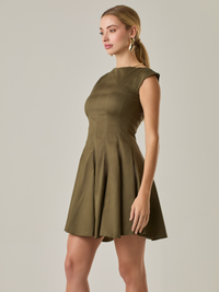 Vestido corto con silueta entallada en la parte superior y falda amplia. Tiene cuello cerrado tipo caja, mangas pequeñas que apenas cubren los hombros y costuras que definen la estructura del torso. La falda incorpora pliegues profundos que le dan volumen y movimiento. El largo llega por encima de la rodilla. Cierre invisible en la espalda.

Detalles:

Color: Olivo