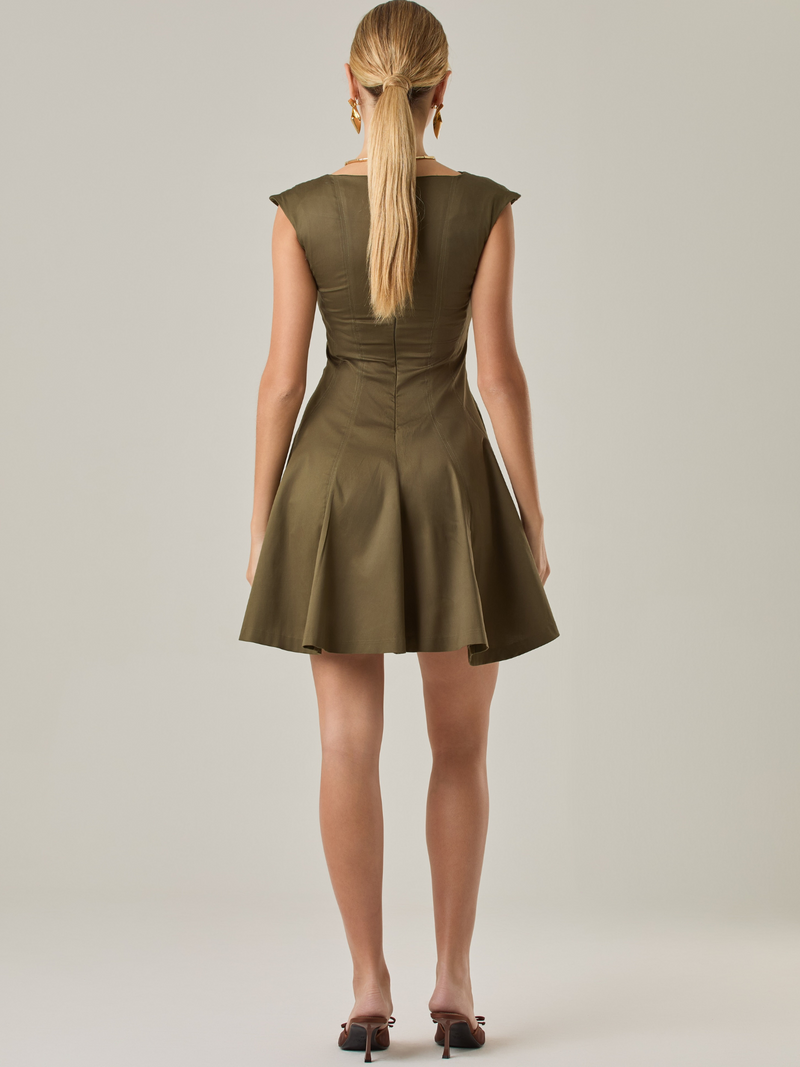Vestido corto con silueta entallada en la parte superior y falda amplia. Tiene cuello cerrado tipo caja, mangas pequeñas que apenas cubren los hombros y costuras que definen la estructura del torso.