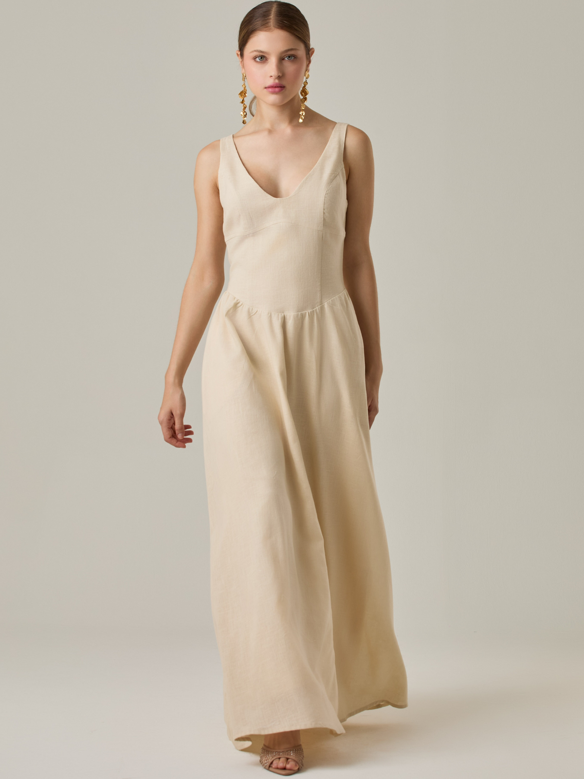 Vestido largo sin mangas con escote sutilmente curvado. El talle entallado contrasta con la amplitud de la falda, creando una silueta fluida y elegante. Una propuesta fresca, pensada para climas cálidos o eventos al aire libre, con un aire relajado que no pierde sofisticación.