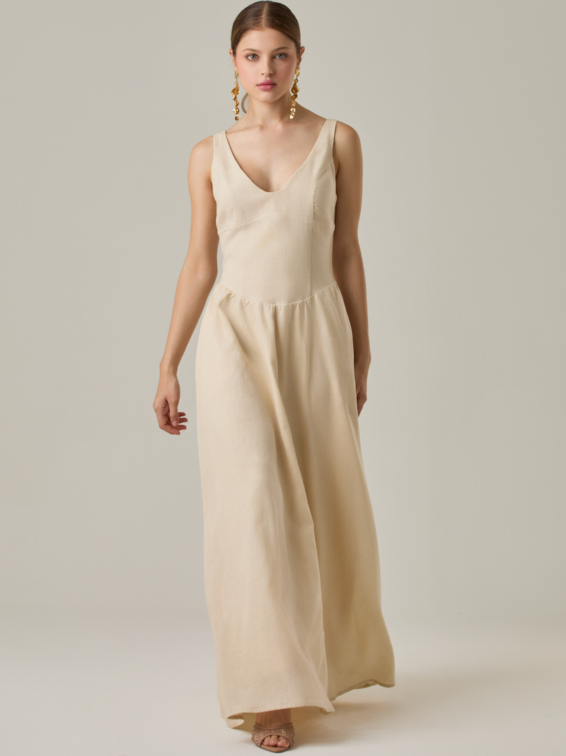 Vestido largo sin mangas con escote sutilmente curvado. El talle entallado contrasta con la amplitud de la falda, creando una silueta fluida y elegante. Una propuesta fresca, pensada para climas cálidos o eventos al aire libre, con un aire relajado que no pierde sofisticación.