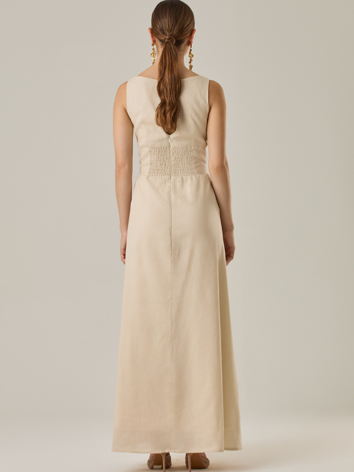 Vestido largo sin mangas con escote sutilmente curvado. El talle entallado contrasta con la amplitud de la falda, creando una silueta fluida y elegante. Una propuesta fresca, pensada para climas cálidos o eventos al aire libre, con un aire relajado que no pierde sofisticación.