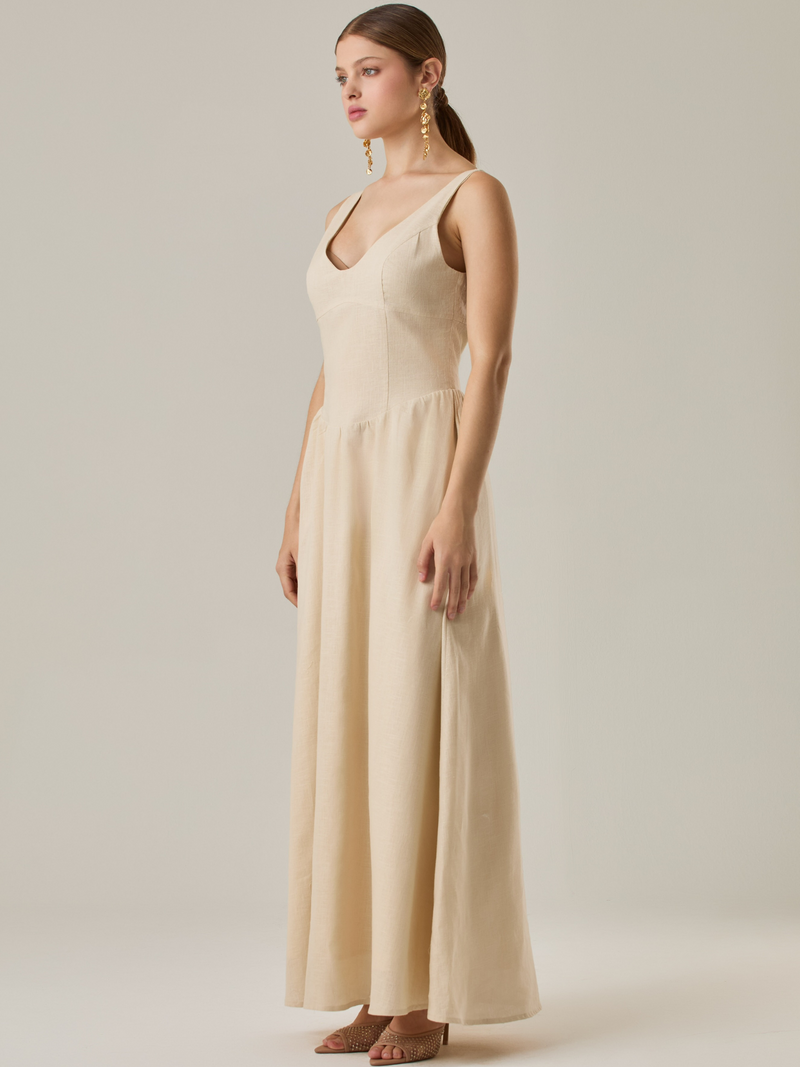 Vestido largo sin mangas con escote sutilmente curvado. El talle entallado contrasta con la amplitud de la falda, creando una silueta fluida y elegante. Una propuesta fresca, pensada para climas cálidos o eventos al aire libre, con un aire relajado que no pierde sofisticación.