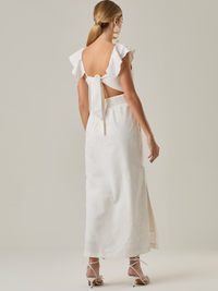 ste vestido tiene un aire delicado y femenino. Es de largo midi, con escote en “V” profundo al frente y en la espalda, y detalles de volantes en los tirantes. La parte trasera se ajusta con un lazo, dejando una abertura que resalta la cintura. El textil tiene un sutil bordado de hojas y flores, aportando textura sin ser recargado. El corte favorece la silueta y la abertura lateral en la falda añade movimiento al caminar. Ideal para eventos elegantes en climas cálidos.
