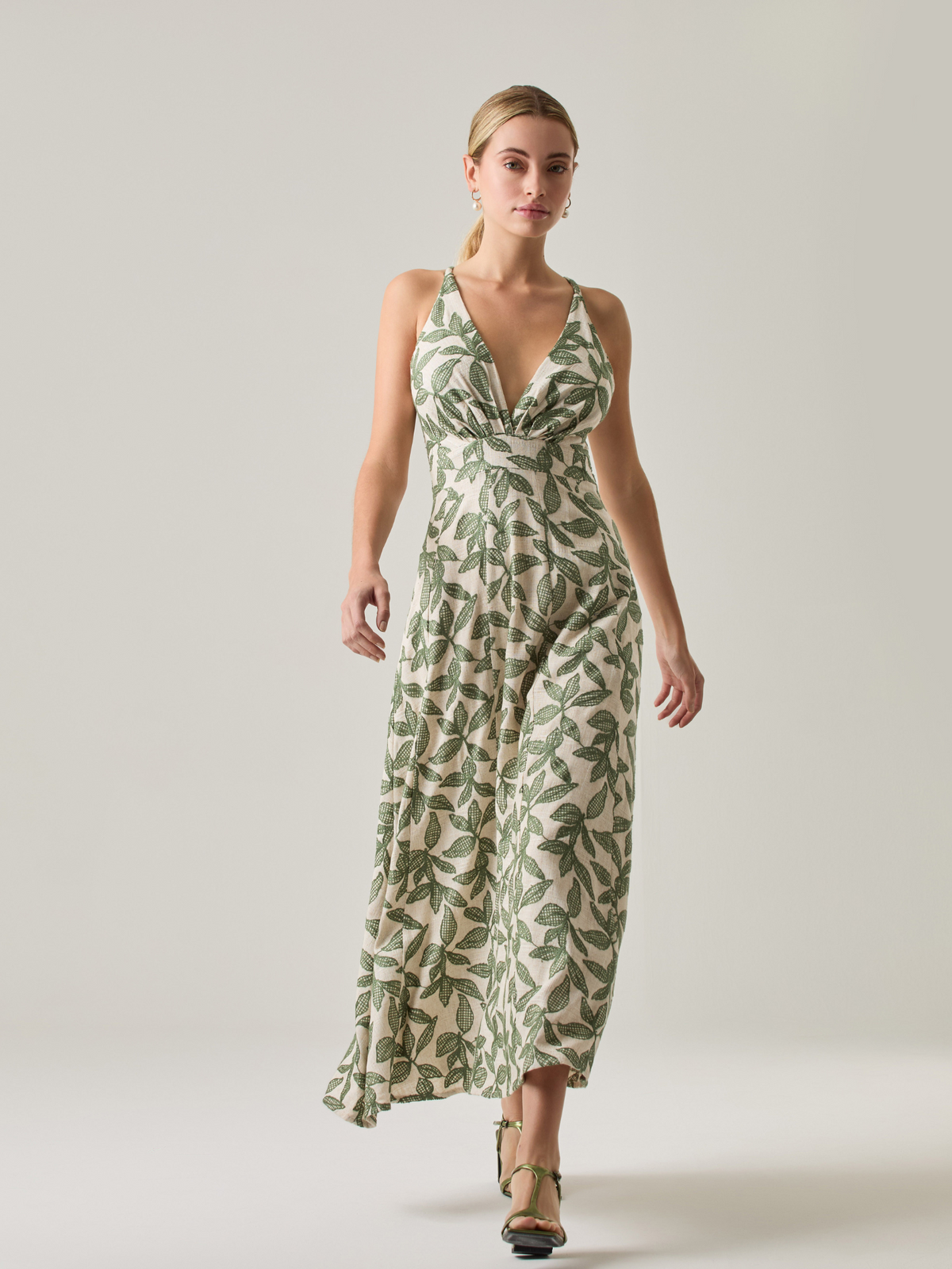 Este vestido largo es una opción fresca y sofisticada. Tiene un escote en V que realza la silueta y tirantes cruzados en la espalda que le dan un toque especial. Su estampado de hojas en tonos verdes resalta sobre la base clara, creando un contraste armonioso. La falda amplia y la cintura ajustable ofrecen comodidad y movimiento, ideal para climas cálidos y ocasiones especiales.