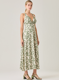 Este vestido largo es una opción fresca y sofisticada. Tiene un escote en V que realza la silueta y tirantes cruzados en la espalda que le dan un toque especial. Su estampado de hojas en tonos verdes resalta sobre la base clara, creando un contraste armonioso. La falda amplia y la cintura ajustable ofrecen comodidad y movimiento, ideal para climas cálidos y ocasiones especiales.