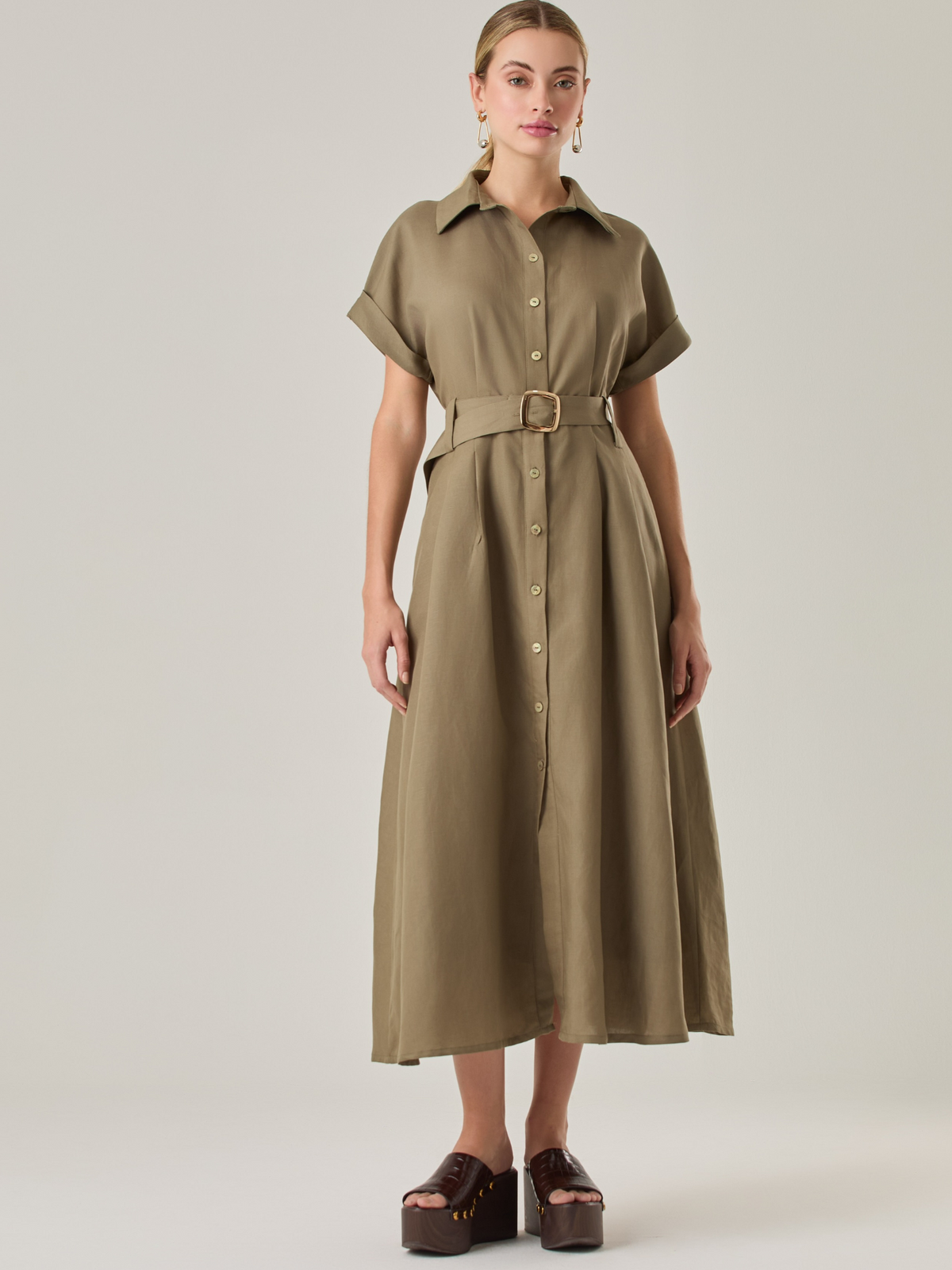 Vestido camisero de silueta midi con botonadura frontal completa y mangas cortas dobladas que aportan un aire relajado. Incorpora un cinturón del mismo material con hebilla forrada que define la cintura y realza la figura. Su estructura lo hace una prenda práctica y atemporal, perfecta para ocasiones casuales o más sofisticadas según cómo se combine.