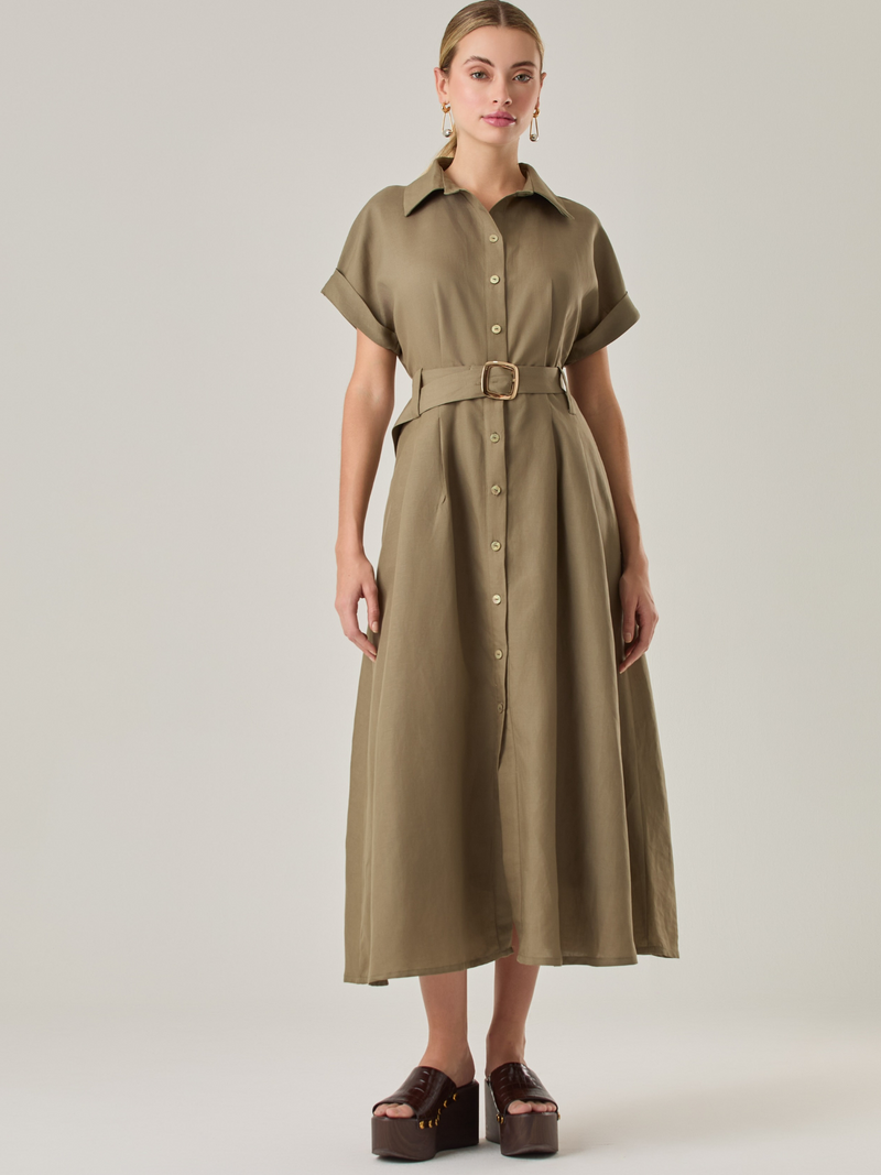 Vestido camisero de silueta midi con botonadura frontal completa y mangas cortas dobladas que aportan un aire relajado. Incorpora un cinturón del mismo material con hebilla forrada que define la cintura y realza la figura. Su estructura lo hace una prenda práctica y atemporal, perfecta para ocasiones casuales o más sofisticadas según cómo se combine.