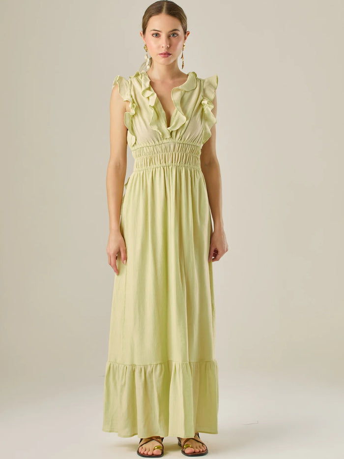 Vestido largo sin mangas con escote en "V" profundo y un diseño con volantes que recorren tanto los tirantes como la parte frontal del busto y la falda. La cintura está fruncida con elástico para dar definición y comodidad, mientras que la falda fluye suavemente con un detalle de volante en el dobladillo, aportando movimiento y un aire femenino al conjunto.