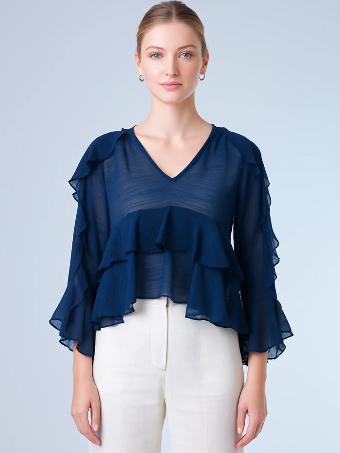 Ligera y romántica, esta blusa de textura vaporosa destaca por sus volantes en capas que aportan movimiento y fluidez. El escote en V y las mangas amplias con acabado ondulado añaden un toque delicado y sofisticado. Ideal para ocasiones especiales, cenas o estilismos casuales con un aire femenino y refinado.
