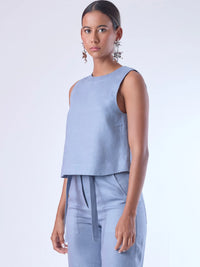 Blusa sin mangas de corte recto y silueta relajada. Tiene cuello redondo cerrado y un diseño limpio sin detalles visibles, lo que le da un estilo minimalista y moderno. El largo llega justo a la cintura, ideal para llevar por fuera o combinada con prendas de talle alto para un look fresco y sofisticado