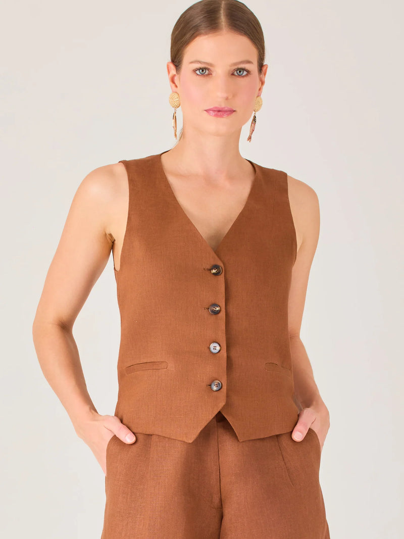Esta blusa tipo chaleco es ideal para climas cálidos o para crear looks sofisticados con un aire casual. Presenta un corte recto ligeramente entallado que acentúa la silueta de forma sutil, y un escote en “V” que estiliza el cuello. Cuenta con una botonadura frontal compuesta por cinco botones oscuros que contrastan elegantemente con el tono neutro de la prenda. También incorpora bolsillos falsos decorativos a ambos lados del frente, que añaden un detalle sutil al diseño minimalista. Esta pieza es versátil 