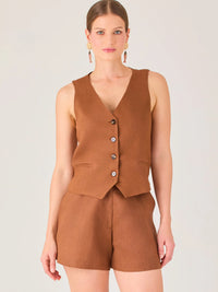 Esta blusa tipo chaleco es ideal para climas cálidos o para crear looks sofisticados con un aire casual. Presenta un corte recto ligeramente entallado que acentúa la silueta de forma sutil, y un escote en “V” que estiliza el cuello. Cuenta con una botonadura frontal compuesta por cinco botones oscuros que contrastan elegantemente con el tono neutro de la prenda. También incorpora bolsillos falsos decorativos a ambos lados del frente, que añaden un detalle sutil al diseño minimalista. Esta pieza es versátil 