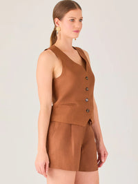 Esta blusa tipo chaleco es ideal para climas cálidos o para crear looks sofisticados con un aire casual. Presenta un corte recto ligeramente entallado que acentúa la silueta de forma sutil, y un escote en “V” que estiliza el cuello. Cuenta con una botonadura frontal compuesta por cinco botones oscuros que contrastan elegantemente con el tono neutro de la prenda. También incorpora bolsillos falsos decorativos a ambos lados del frente, que añaden un detalle sutil al diseño minimalista. Esta pieza es versátil 