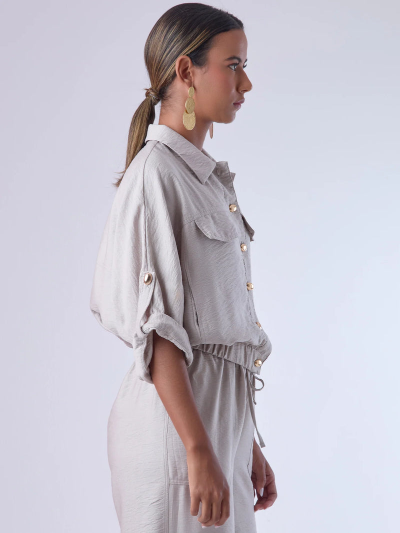 Relajada pero estructurada, esta blusa de silueta amplia combina un diseño utilitario con detalles refinados. Presenta bolsillos de solapa en el pecho, mangas con opción de ajuste y una botonadura dorada que aporta un toque de brillo sutil. Ideal para estilismos casuales con elegancia natural, o para elevar conjuntos relajados con una prenda clave y atemporal.