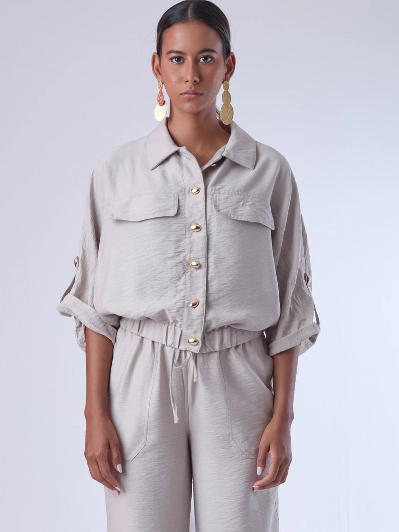 Relajada pero estructurada, esta blusa de silueta amplia combina un diseño utilitario con detalles refinados. Presenta bolsillos de solapa en el pecho, mangas con opción de ajuste y una botonadura dorada que aporta un toque de brillo sutil. Ideal para estilismos casuales con elegancia natural, o para elevar conjuntos relajados con una prenda clave y atemporal.