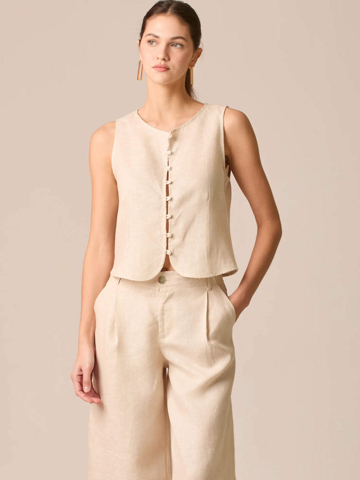 Blusa tipo chaleco sin mangas, con escote redondo y cierre frontal de botones forrados, entallada en la parte superior y con dobladillo ligeramente curvado que aporta un acabado elegante y estructurado