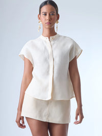 Blusa de silueta recta con manga corta tipo caída y estructura relajada. Cuenta con cuello que se cierra con un pequeño broche metálico decorativos estilo sobrio la hace versátil y elegante, ideal para atuendos casuales o más refinados.