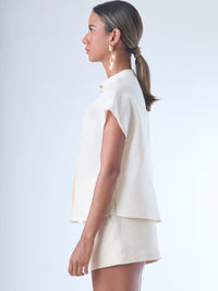 Blusa de silueta recta con manga corta tipo caída y estructura relajada. Cuenta con cuello que se cierra con un pequeño broche metálico decorativos estilo sobrio la hace versátil y elegante, ideal para atuendos casuales o más refinados.