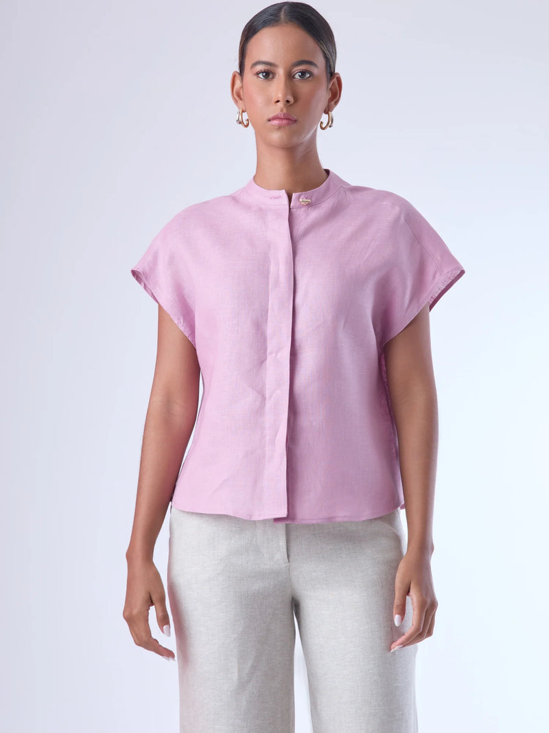 Blusa de silueta recta con manga corta tipo caída y estructura relajada. Cuenta con cuello que se cierra con un pequeño broche metálico decorativos estilo sobrio la hace versátil y elegante, ideal para atuendos casuales o más refinados.