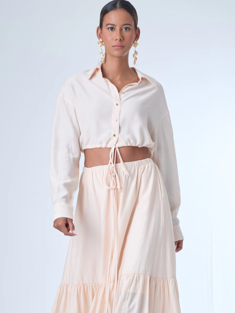 Blusa de corte relajado y largo cropped, con manga larga y puños con botones. Tiene cuello clásico camisero y una botonadura frontal. La prenda se ajusta a la cintura mediante un ligero fruncido con cordón interno, creando un efecto ablusado. Su estilo es casual con un toque sofisticado y femenino.

Detalles:

Color: Curuba

Material:18% Nylon 82% Rayón