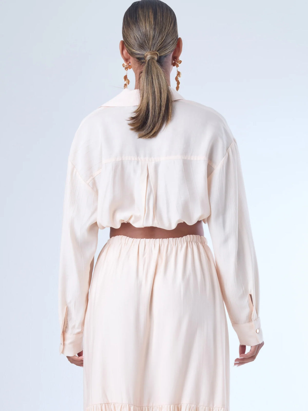 Blusa de corte relajado y largo cropped, con manga larga y puños con botones. Tiene cuello clásico camisero y una botonadura frontal. La prenda se ajusta a la cintura mediante un ligero fruncido con cordón interno, creando un efecto ablusado. Su estilo es casual con un toque sofisticado y femenino.

Detalles:

Color: Curuba

Material:18% Nylon 82% Rayón