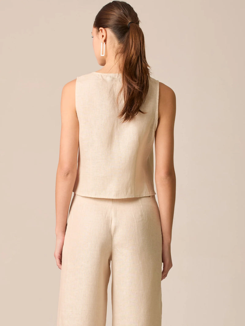 Blusa tipo chaleco sin mangas, con escote redondo y cierre frontal de botones forrados, entallada en la parte superior y con dobladillo ligeramente curvado que aporta un acabado elegante y estructurado