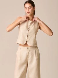 Blusa tipo chaleco sin mangas, con escote redondo y cierre frontal de botones forrados, entallada en la parte superior y con dobladillo ligeramente curvado que aporta un acabado elegante y estructurado