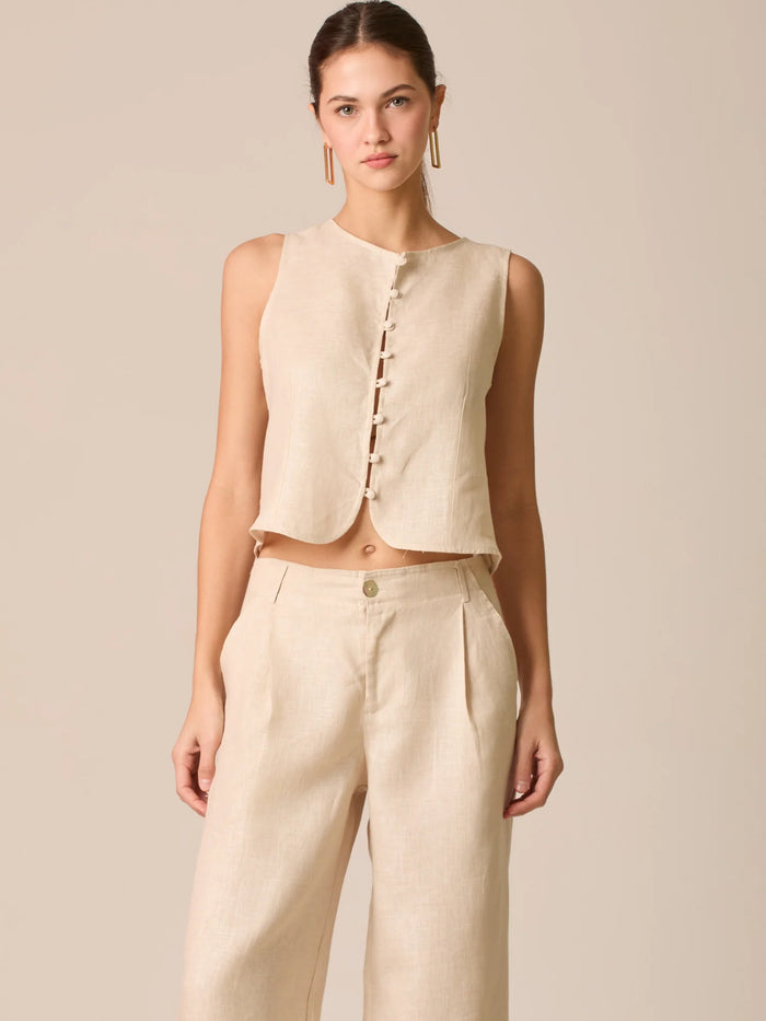 Blusa tipo chaleco sin mangas, con escote redondo y cierre frontal de botones forrados, entallada en la parte superior y con dobladillo ligeramente curvado que aporta un acabado elegante y estructurado