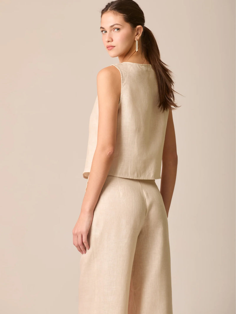 Blusa tipo chaleco sin mangas, con escote redondo y cierre frontal de botones forrados, entallada en la parte superior y con dobladillo ligeramente curvado que aporta un acabado elegante y estructurado