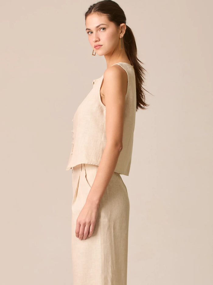 Blusa tipo chaleco sin mangas, con escote redondo y cierre frontal de botones forrados, entallada en la parte superior y con dobladillo ligeramente curvado que aporta un acabado elegante y estructurado