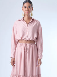 Blusa de corte relajado y largo cropped, con manga larga y puños con botones. Tiene cuello clásico camisero y una botonadura frontal. La prenda se ajusta a la cintura mediante un ligero fruncido con cordón interno, creando un efecto ablusado. Su estilo es casual con un toque sofisticado y femenino.

Detalles:

Color: Rosa