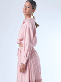 Blusa de corte relajado y largo cropped, con manga larga y puños con botones. Tiene cuello clásico camisero y una botonadura frontal. La prenda se ajusta a la cintura mediante un ligero fruncido con cordón interno, creando un efecto ablusado. Su estilo es casual con un toque sofisticado y femenino.

Detalles:

Color: Rosa