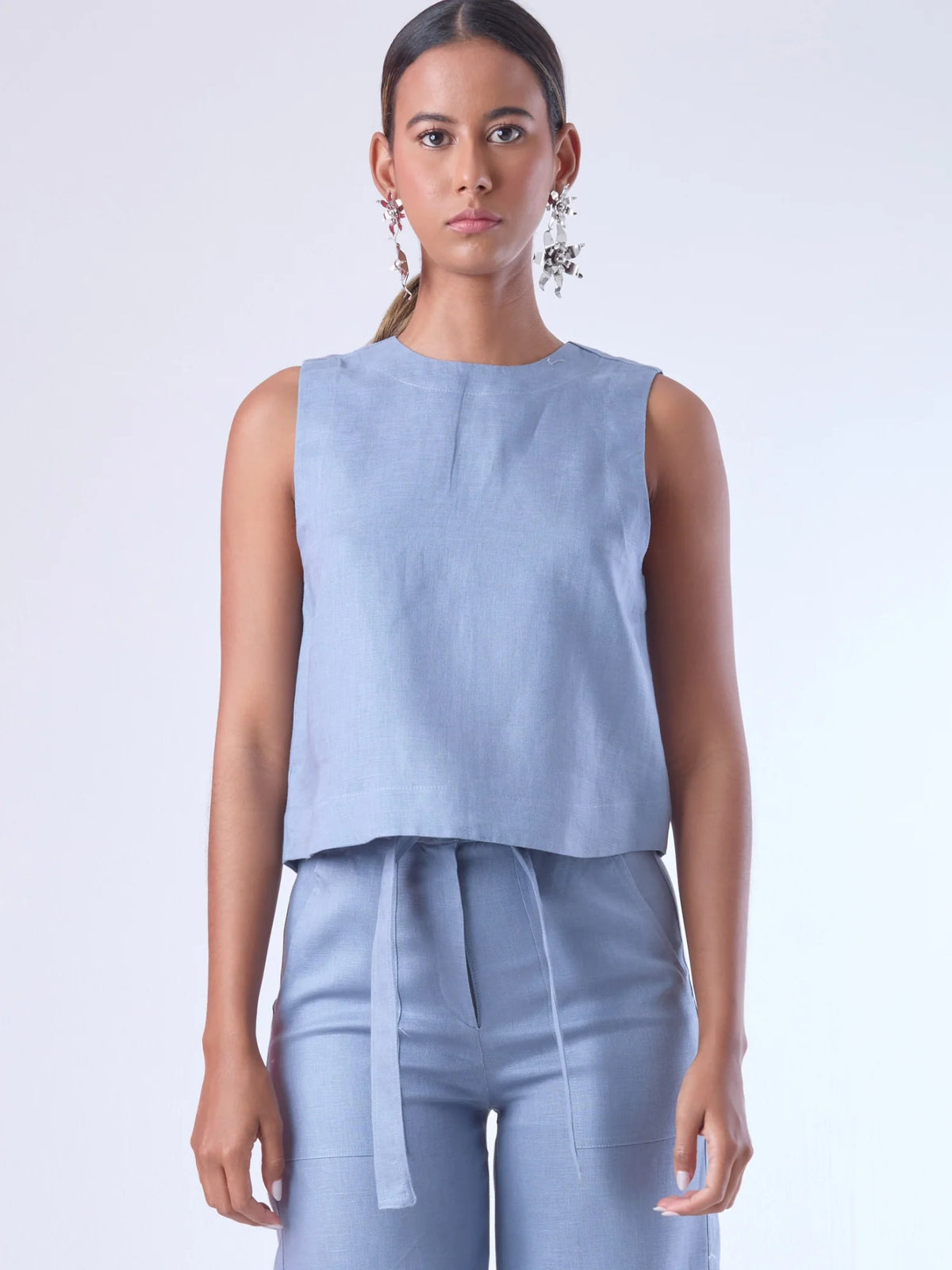 Blusa sin mangas de corte recto y silueta relajada. Tiene cuello redondo cerrado y un diseño limpio sin detalles visibles, lo que le da un estilo minimalista y moderno. El largo llega justo a la cintura, ideal para llevar por fuera o combinada con prendas de talle alto para un look fresco y sofisticado