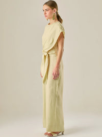 Este enterizo presenta un diseño elegante y minimalista, ideal para ocasiones casuales con estilo o eventos diurnos sofisticados. Confeccionado en un tono beige claro, tiene un corte relajado con mangas tipo kimono, cuello redondo y un diseño limpio sin botones ni cierres visibles en el frente. La prenda se ajusta en la cintura con un cinturón del mismo tejido, que se anuda al frente, creando una silueta favorecedora. El pantalón es de pierna ancha y caída fluida, lo que aporta comodidad y movimiento. Compl