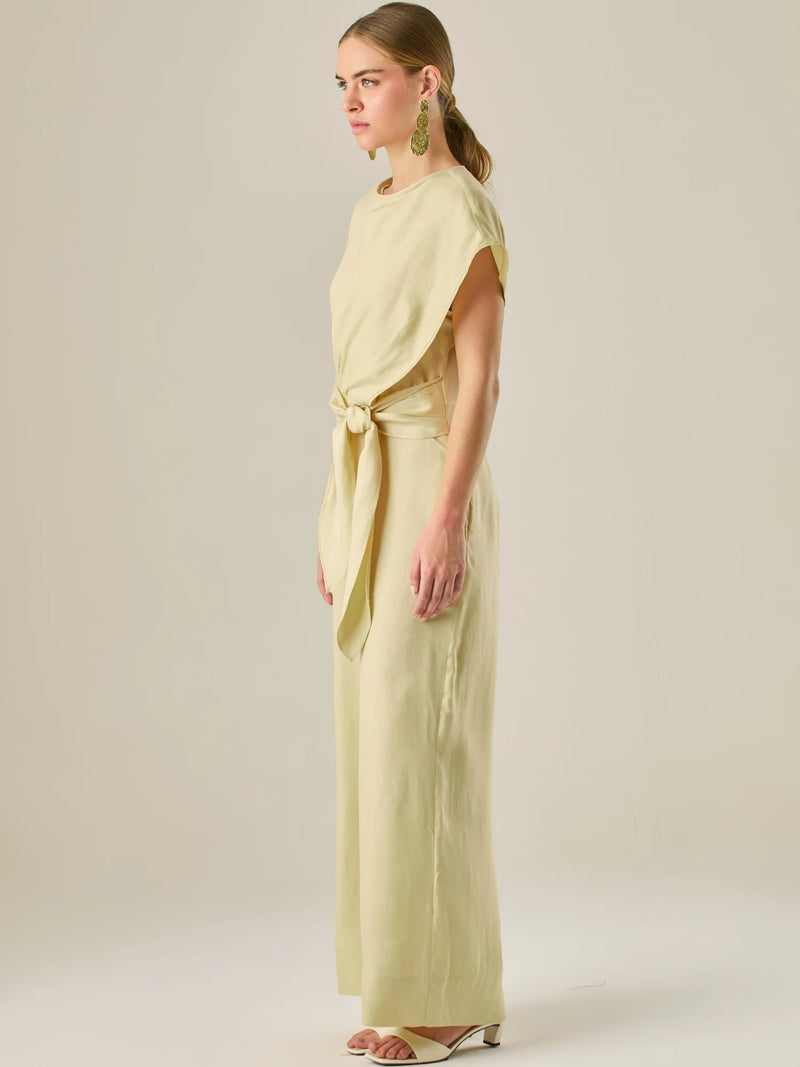 Este enterizo presenta un diseño elegante y minimalista, ideal para ocasiones casuales con estilo o eventos diurnos sofisticados. Confeccionado en un tono beige claro, tiene un corte relajado con mangas tipo kimono, cuello redondo y un diseño limpio sin botones ni cierres visibles en el frente. La prenda se ajusta en la cintura con un cinturón del mismo tejido, que se anuda al frente, creando una silueta favorecedora. El pantalón es de pierna ancha y caída fluida, lo que aporta comodidad y movimiento. Compl