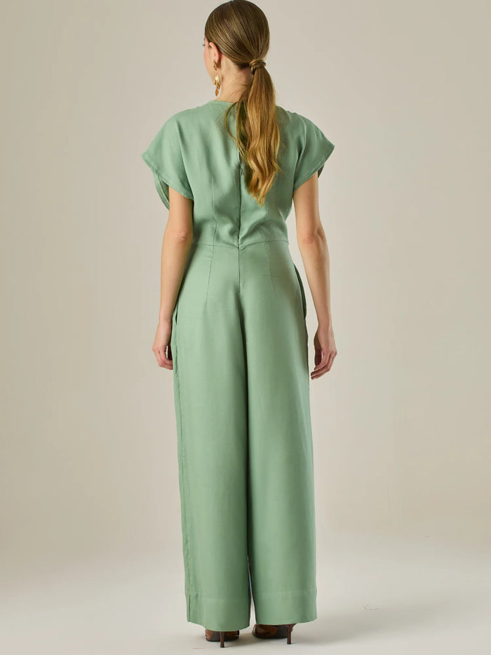 Este enterizo presenta un diseño elegante y minimalista, ideal para ocasiones casuales con estilo o eventos diurnos sofisticados. Confeccionado en un tono beige claro, tiene un corte relajado con mangas tipo kimono, cuello redondo y un diseño limpio sin botones ni cierres visibles en el frente. La prenda se ajusta en la cintura con un cinturón del mismo tejido, que se anuda al frente, creando una silueta favorecedora. El pantalón es de pierna ancha y caída fluida, lo que aporta comodidad y movimiento. Compl