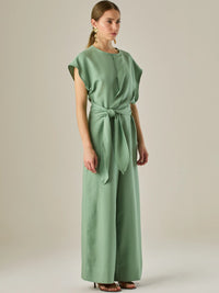 Este enterizo presenta un diseño elegante y minimalista, ideal para ocasiones casuales con estilo o eventos diurnos sofisticados. Confeccionado en un tono beige claro, tiene un corte relajado con mangas tipo kimono, cuello redondo y un diseño limpio sin botones ni cierres visibles en el frente. La prenda se ajusta en la cintura con un cinturón del mismo tejido, que se anuda al frente, creando una silueta favorecedora. El pantalón es de pierna ancha y caída fluida, lo que aporta comodidad y movimiento. Compl