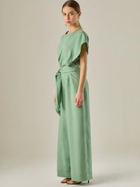 Este enterizo presenta un diseño elegante y minimalista, ideal para ocasiones casuales con estilo o eventos diurnos sofisticados. Confeccionado en un tono beige claro, tiene un corte relajado con mangas tipo kimono, cuello redondo y un diseño limpio sin botones ni cierres visibles en el frente. La prenda se ajusta en la cintura con un cinturón del mismo tejido, que se anuda al frente, creando una silueta favorecedora. El pantalón es de pierna ancha y caída fluida, lo que aporta comodidad y movimiento. Compl