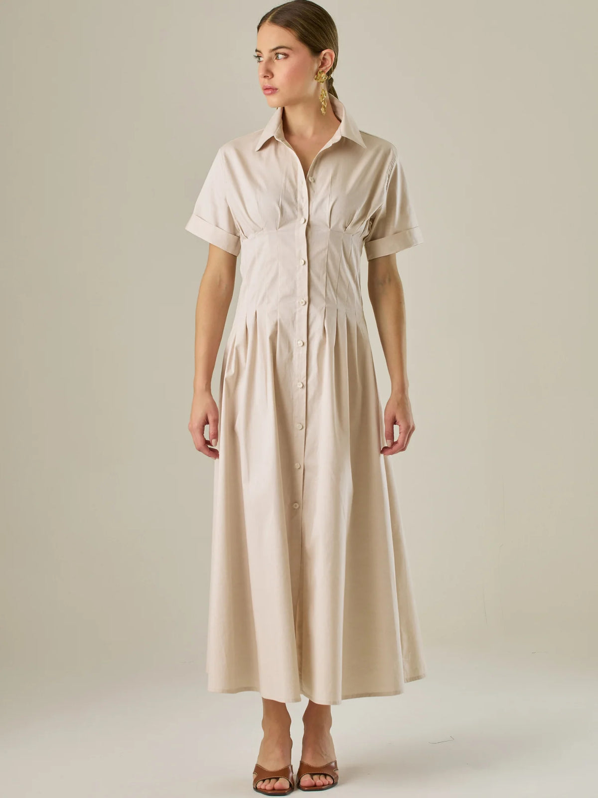 Vestido camisero midi con mangas cortas y falda amplia, ideal para un look elegante y relajado. Su diseño con pinzas en el busto realza la figura con sutileza, mientras que los botones al frente aportan un toque clásico y versátil.

Detalles:

Color: Sand

Material: 97% Algodón 3% Spandex