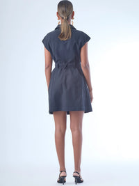 Vestido corto de estilo camisero con botones grandes al frente. Cuenta con cuello clásico, mangas cortas tipo casquillo y bolsillos de parche en el pecho y la parte baja del frente, que aportan un aire utilitario. La cintura se ajusta con un cinturón del mismo tejido, creando una silueta definida. Su diseño combina funcionalidad y sofisticación de manera equilibrada.

Detalles:

Color: Negro