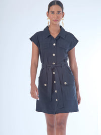 Vestido corto de estilo camisero con botones grandes al frente. Cuenta con cuello clásico, mangas cortas tipo casquillo y bolsillos de parche en el pecho y la parte baja del frente, que aportan un aire utilitario. La cintura se ajusta con un cinturón del mismo tejido, creando una silueta definida. Su diseño combina funcionalidad y sofisticación de manera equilibrada.

Detalles:

Color: Negro