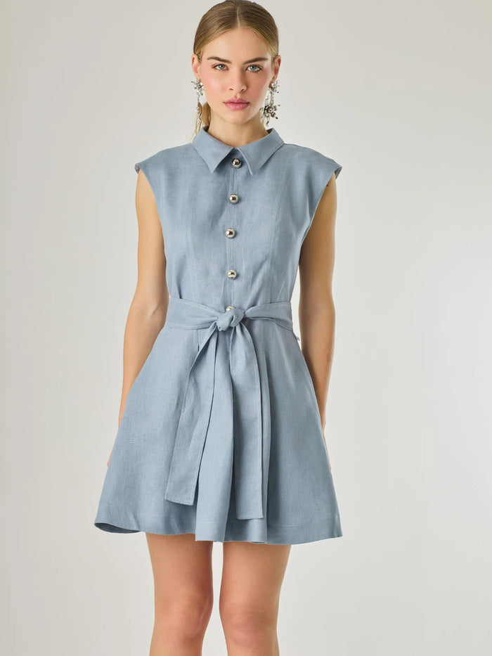 Vestido corto sin mangas con botones frontales y cuello camisero, complementado con un lazo que define la cintura. Su diseño sencillo y femenino lo convierte en una opción ideal para un look casual con un aire sofisticado y fresco.

Color: Indigo

Material: Lino

Características: Incluye cinturón a tono.