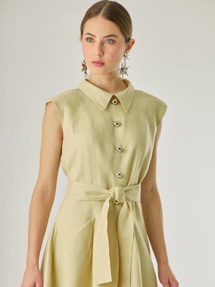 Vestido corto sin mangas con botones frontales y cuello camisero, complementado con un lazo que define la cintura. Su diseño sencillo y femenino lo convierte en una opción ideal para un look casual con un aire sofisticado y fresco.

Color: Vainilla

Material: Lino