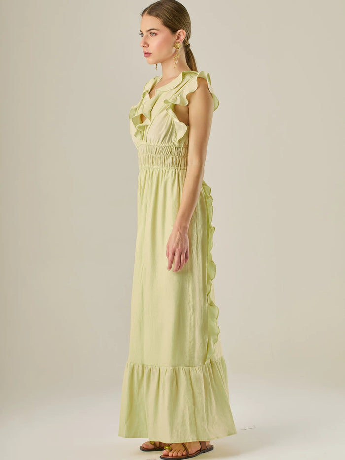 Vestido largo sin mangas con escote en "V" profundo y un diseño con volantes que recorren tanto los tirantes como la parte frontal del busto y la falda. La cintura está fruncida con elástico para dar definición y comodidad, mientras que la falda fluye suavemente con un detalle de volante en el dobladillo, aportando movimiento y un aire femenino al conjunto.