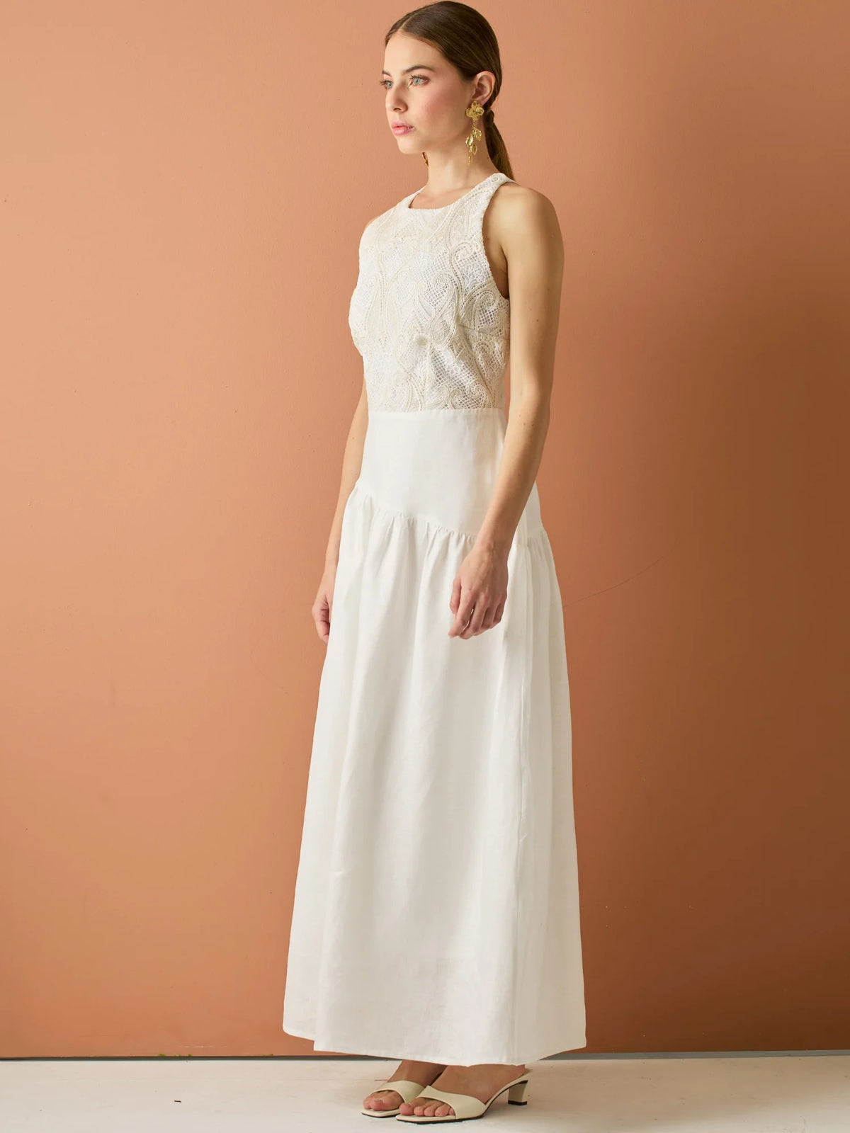 Vestido largo sin mangas con escote halter y cuerpo bordado en delicado encaje. La falda de lino con caída fluida aporta frescura y movimiento, creando una silueta femenina y elegante ideal para ocasiones especiales con un aire natural y sofisticado.