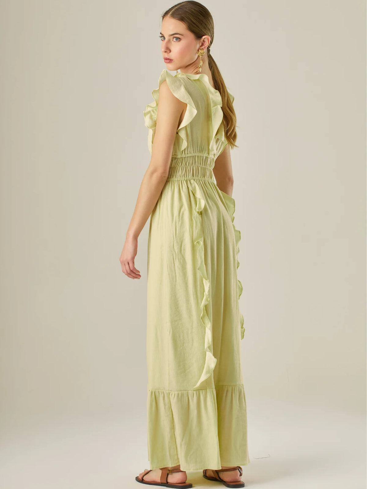 Vestido largo sin mangas con escote en "V" profundo y un diseño con volantes que recorren tanto los tirantes como la parte frontal del busto y la falda. La cintura está fruncida con elástico para dar definición y comodidad, mientras que la falda fluye suavemente con un detalle de volante en el dobladillo, aportando movimiento y un aire femenino al conjunto.
