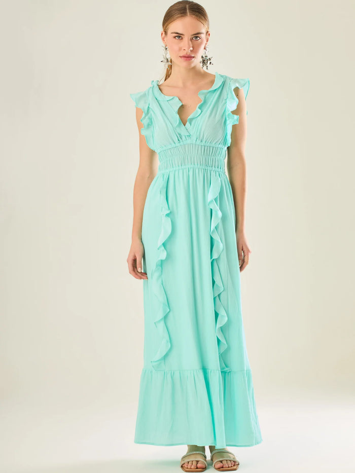 Vestido largo sin mangas con escote en "V" profundo y un diseño con volantes que recorren tanto los tirantes como la parte frontal del busto y la falda. La cintura está fruncida con elástico para dar definición y comodidad, mientras que la falda fluye suavemente con un detalle de volante en el dobladillo, aportando movimiento y un aire femenino al conjunto.